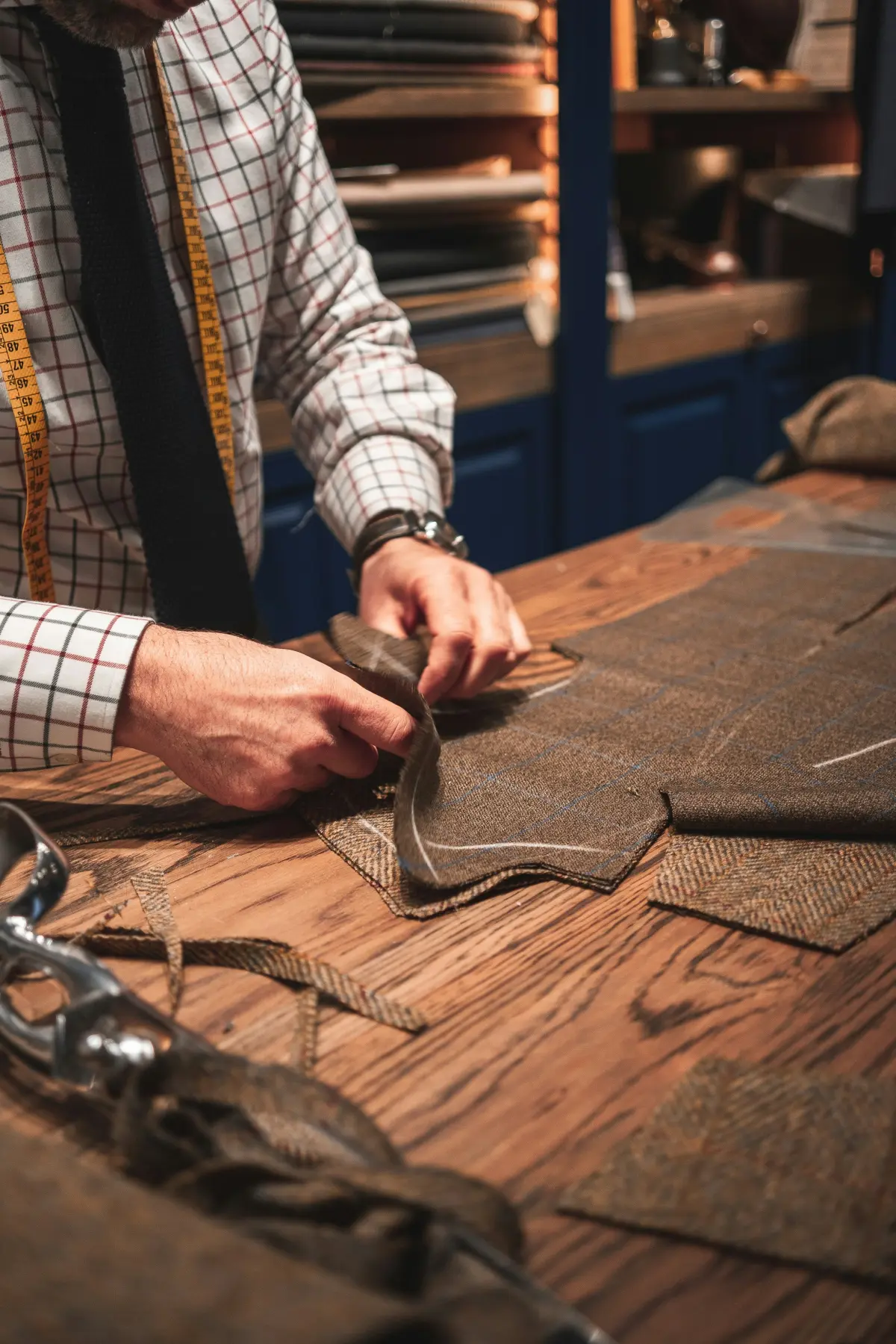 Tailor cutting tweed fabric on a wooden workbench with measuring tape and scissors